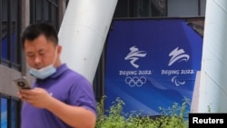 资料照:2021年7月30日,在北京奥组委总部,一名男子在走过北京2022年冬奥会和冬残奥会的标志时使用手机。