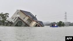 中国江西省上饶市鄱阳湖附近地区被洪水淹没,几人划着小船经过一所被洪水冲倒的民宅。(2020年7月15日)