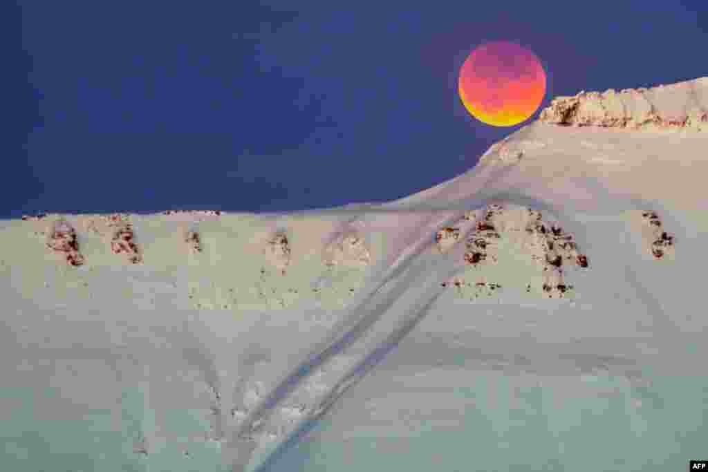 2018年1月31日,从挪威斯瓦尔巴群岛的朗伊尔城(Longyearbyen)可以看到雪山之巅的红黄相间的明月。