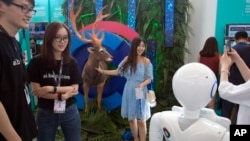 2018年7月4日在北京举行的2018百度AI开发者大会期间,一名女子在鹿的复制品旁边摆拍,尝试机器视觉识别仪器。该活动旨在将开发商,企业和个人同百度的人工智能资源联系起来。