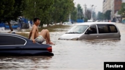 2021 年 7 月 22 日,中国河南省郑州市暴雨过后,一名男子坐在被淹道路上的滞留车辆上。(路透社照片)