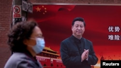 2020年3月12日,新冠病毒爆发期间,一名戴口罩的妇女从上海街头的一副中国国家主席习近平的宣传图像前走过。