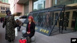 2014年5月1日,一位维吾尔妇女坐在乌鲁木齐街头,身后是铁笼保护下的中国武警。