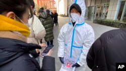 2022年1月26日(周三),一名身穿防护服的工作人员手持印有“北京健康码”的二维码的纸,在北京一家私人冠状病毒检测中心进行检测。