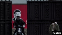 戴着口罩的行人从上海街头一个有着习近平画像的大门前经过。(2020年2月10日)